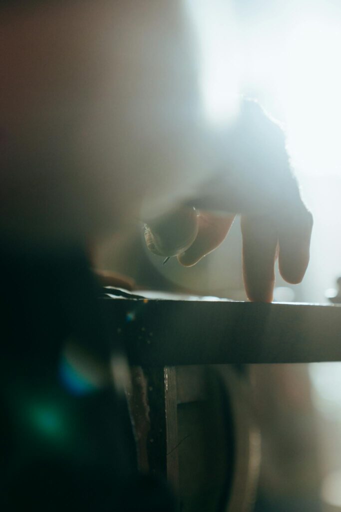 Artist's hand in dramatic light crafting wooden object at workshop.